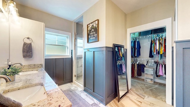 bathroom featuring a shower stall, wainscoting, a walk in closet, and a sink