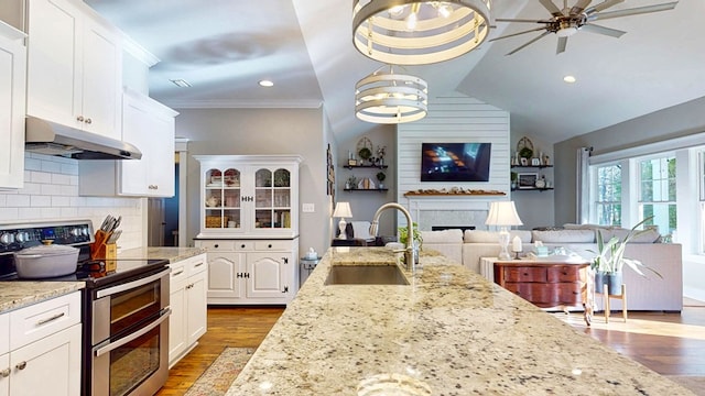 kitchen featuring tasteful backsplash, under cabinet range hood, range with two ovens, a fireplace, and a sink