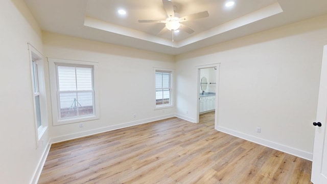 unfurnished room featuring a raised ceiling, light wood-type flooring, and ceiling fan