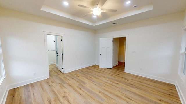 unfurnished room with ceiling fan, light wood-type flooring, and a raised ceiling