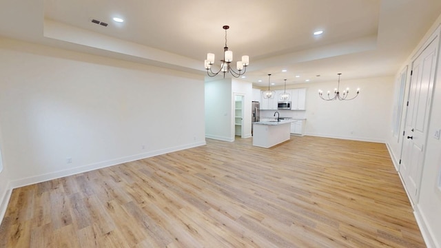 interior space featuring a tray ceiling, an island with sink, hanging light fixtures, and an inviting chandelier