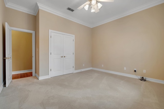 unfurnished bedroom featuring crown molding, light colored carpet, ceiling fan, and a closet