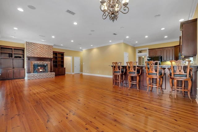 unfurnished living room with an inviting chandelier, ornamental molding, a brick fireplace, and light wood-type flooring