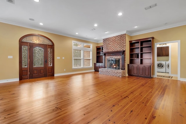 unfurnished living room featuring separate washer and dryer, a brick fireplace, ornamental molding, and light hardwood / wood-style floors