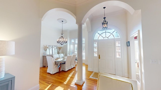 entryway featuring decorative columns, a high ceiling, a notable chandelier, light hardwood / wood-style floors, and crown molding