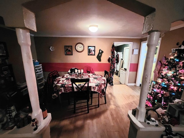 dining space with hardwood / wood-style flooring, crown molding, and ornate columns