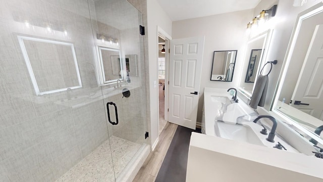 bathroom featuring double vanity, wood finished floors, a stall shower, and a sink