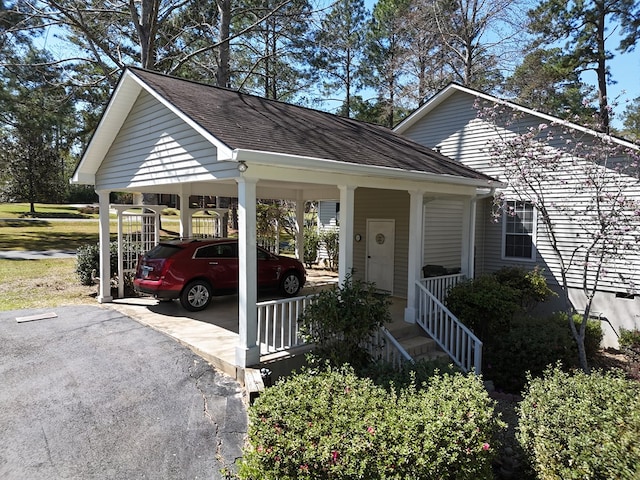 view of front of property with a detached carport, a porch, a shingled roof, and driveway