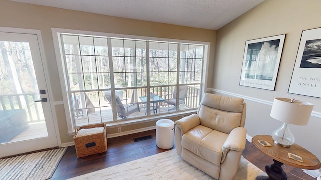 living area featuring plenty of natural light, wood finished floors, visible vents, and vaulted ceiling