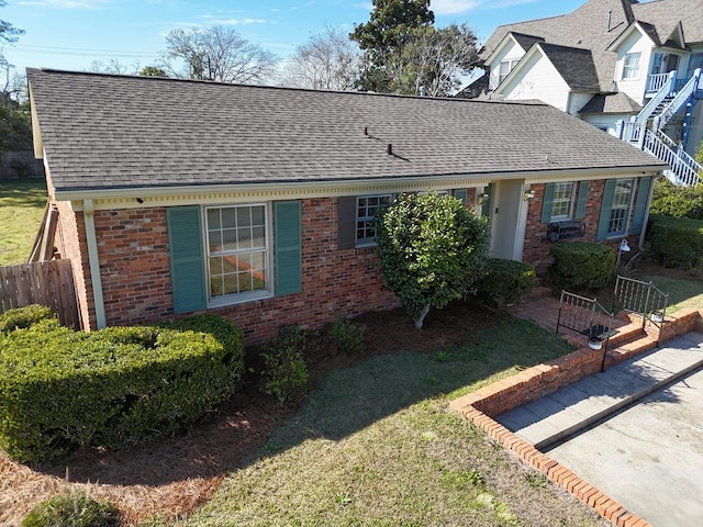 ranch-style home with brick siding, fence, a front lawn, and roof with shingles