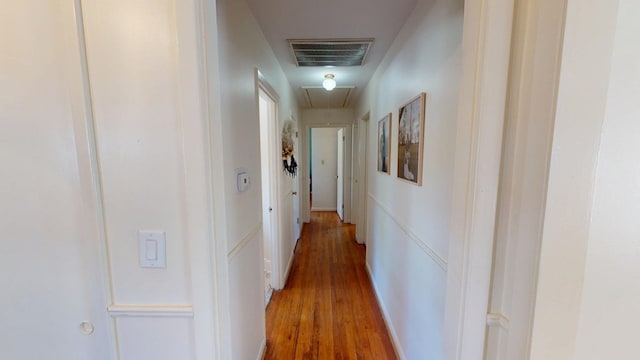 hallway with attic access, visible vents, and light wood-style floors