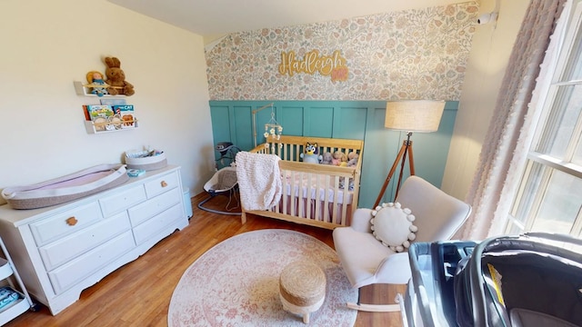 bedroom featuring light wood-type flooring, a wainscoted wall, a nursery area, and wallpapered walls