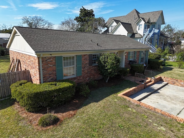 view of front of property with brick siding, roof with shingles, a front yard, and fence