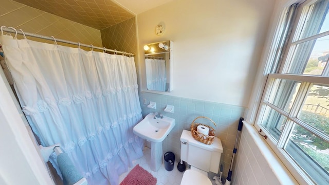 bathroom with tile patterned flooring, toilet, a wainscoted wall, a shower with shower curtain, and tile walls