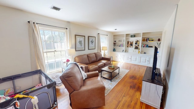 living room featuring wood finished floors, visible vents, and built in features