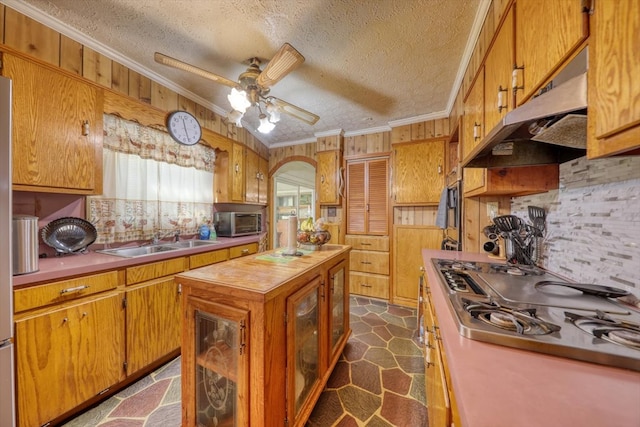 kitchen with sink, wooden walls, gas stovetop, ornamental molding, and a textured ceiling