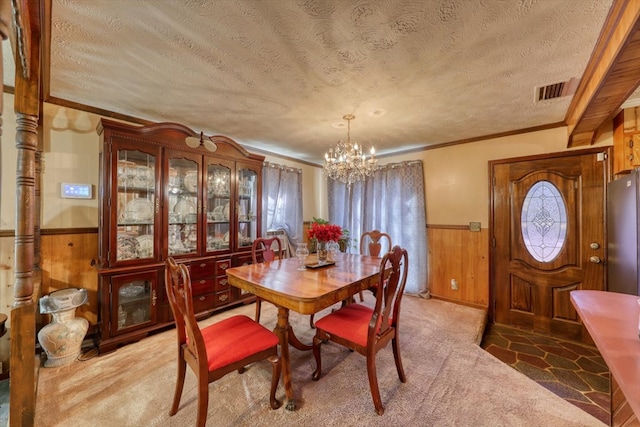 carpeted dining space featuring an inviting chandelier, crown molding, wooden walls, and a textured ceiling