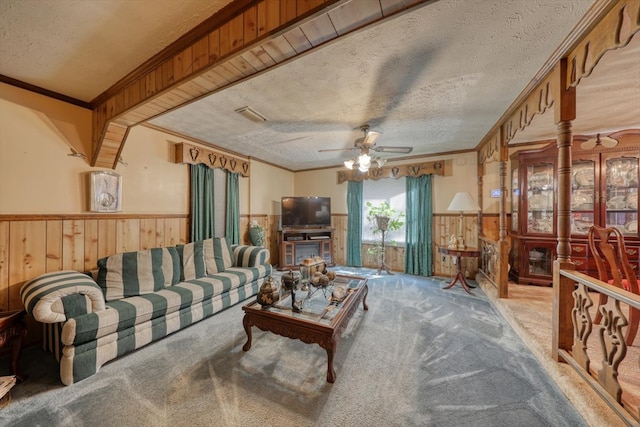 carpeted living room with ceiling fan, ornamental molding, a textured ceiling, and wood walls