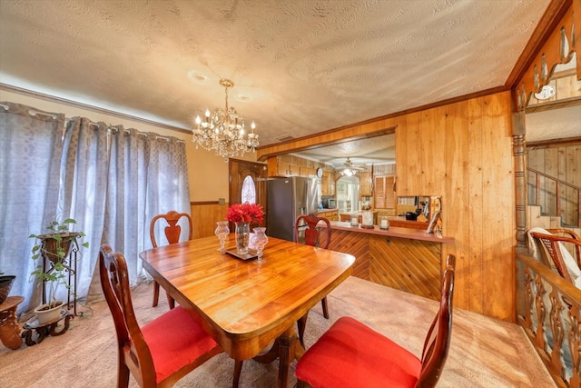 carpeted dining area with wooden walls, a chandelier, and a textured ceiling