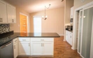 kitchen with light hardwood / wood-style flooring, white cabinets, vaulted ceiling, stainless steel dishwasher, and kitchen peninsula