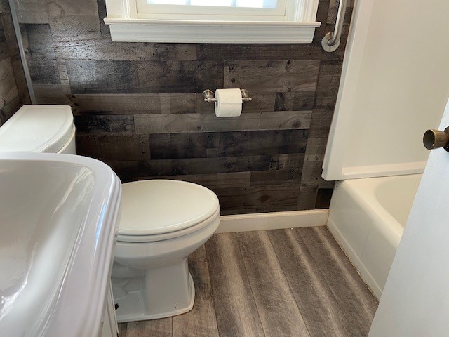 bathroom with wood-type flooring, a tub, wood walls, and toilet