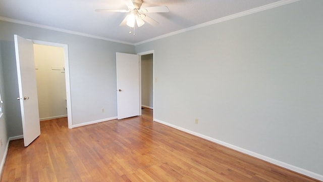 unfurnished bedroom featuring a walk in closet, crown molding, wood finished floors, and baseboards