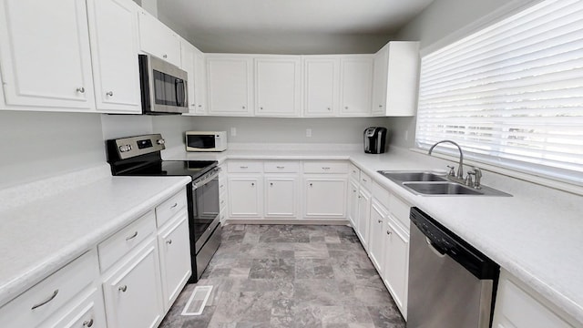 kitchen featuring white cabinets, appliances with stainless steel finishes, light countertops, and a sink