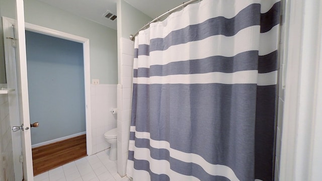 bathroom featuring tile patterned floors, visible vents, toilet, a shower with shower curtain, and tile walls