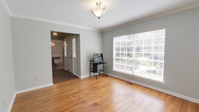 unfurnished room featuring visible vents, wood finished floors, an inviting chandelier, crown molding, and baseboards