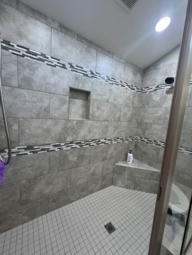 bathroom featuring lofted ceiling and tiled shower