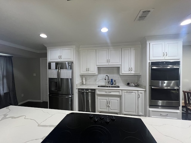 kitchen with sink, white cabinets, stainless steel appliances, light stone countertops, and backsplash