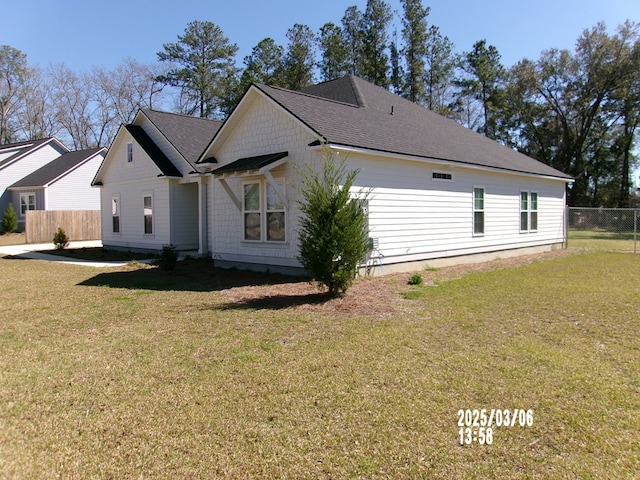 view of side of home with a shingled roof, fence, and a lawn