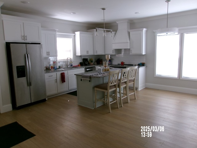 kitchen featuring premium range hood, a kitchen island, a sink, ornamental molding, and stainless steel refrigerator with ice dispenser