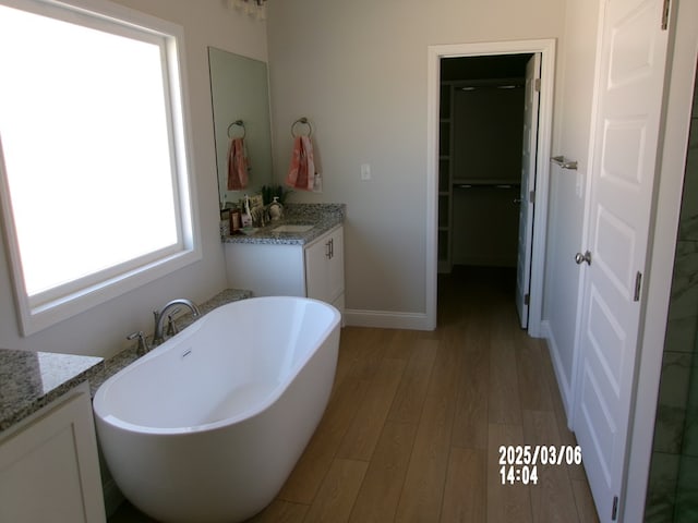 bathroom featuring a soaking tub, baseboards, wood finished floors, and vanity