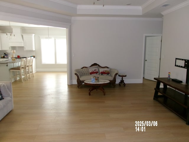 interior space with crown molding, light wood finished floors, a raised ceiling, visible vents, and baseboards