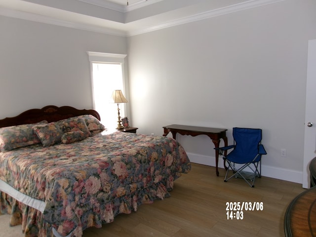 bedroom featuring baseboards, ornamental molding, a raised ceiling, and wood finished floors