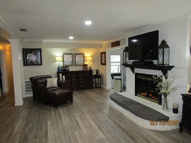 living room with crown molding, wood-type flooring, a fireplace, and decorative columns