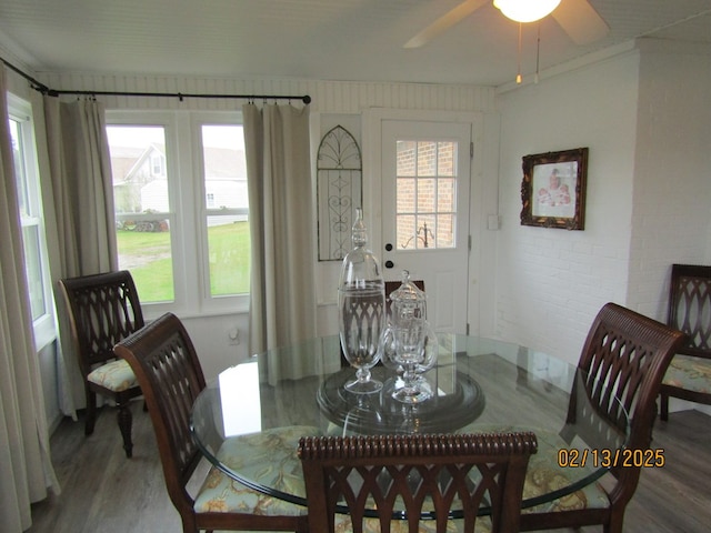 dining area featuring hardwood / wood-style floors, ceiling fan, and brick wall