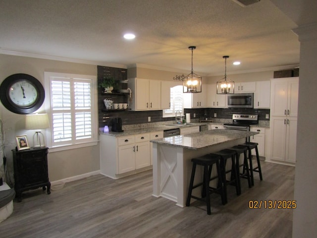 kitchen with white cabinetry, stainless steel appliances, crown molding, and a kitchen island