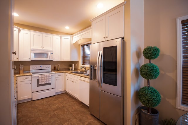 kitchen featuring sink, light stone counters, white cabinets, and white appliances