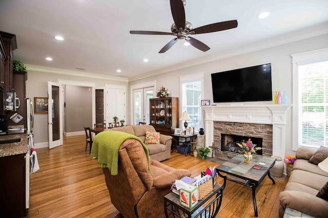 living area with baseboards, light wood-style flooring, crown molding, a fireplace, and recessed lighting