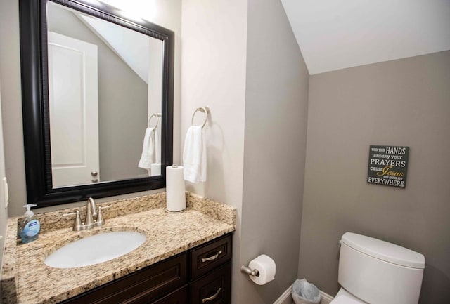 half bathroom featuring lofted ceiling, toilet, and vanity