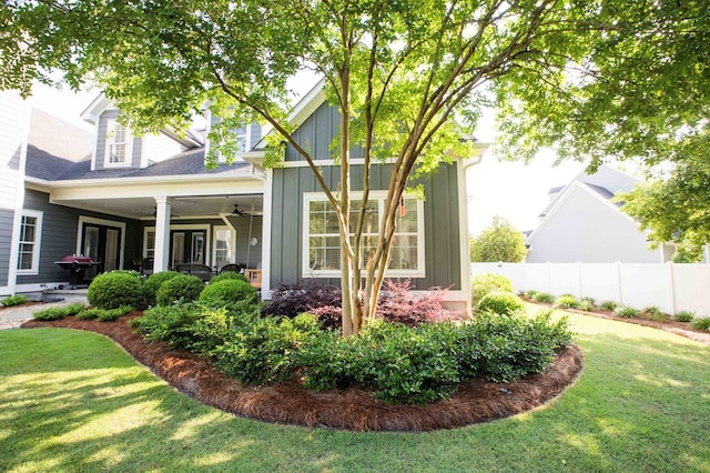 view of side of home featuring a yard, fence, board and batten siding, and a ceiling fan