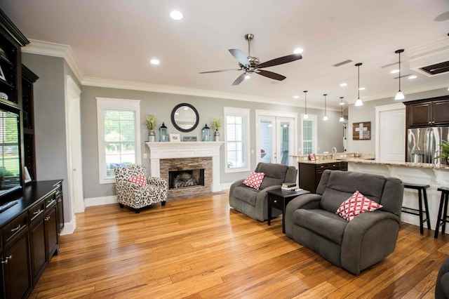 living area featuring light wood-style floors, baseboards, a fireplace, and ornamental molding