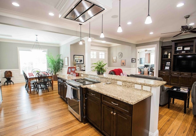 kitchen featuring light wood finished floors, a wainscoted wall, open floor plan, hanging light fixtures, and double oven range