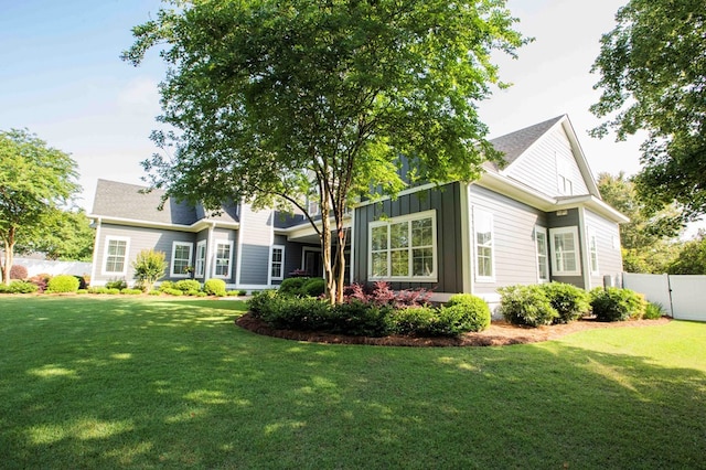 rear view of property featuring board and batten siding, fence, and a lawn