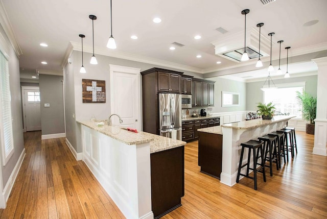 kitchen with stainless steel appliances, light wood-style flooring, ornamental molding, dark brown cabinets, and a kitchen breakfast bar