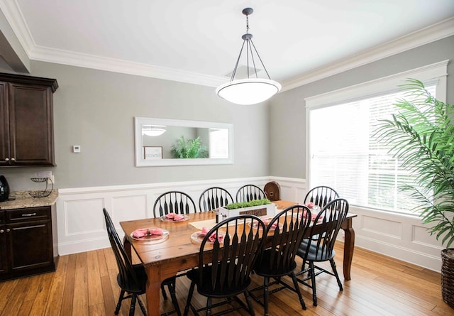 dining space with crown molding, light wood-style flooring, and a decorative wall