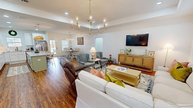 living room featuring recessed lighting, a notable chandelier, a tray ceiling, and dark wood-type flooring