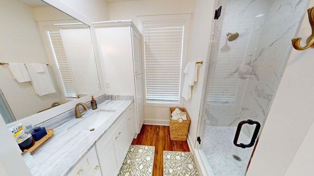 full bathroom featuring vanity, a marble finish shower, baseboards, and wood finished floors
